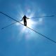 Man silhouetted by the sun and walking across tightrope with balancing pole with a clear sky background